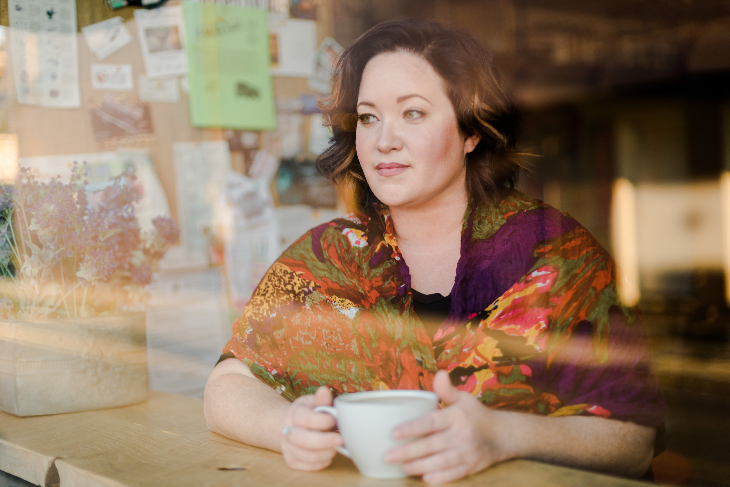 woman sitting in a cafe with a coffee mug gazing out the window during her portrait session