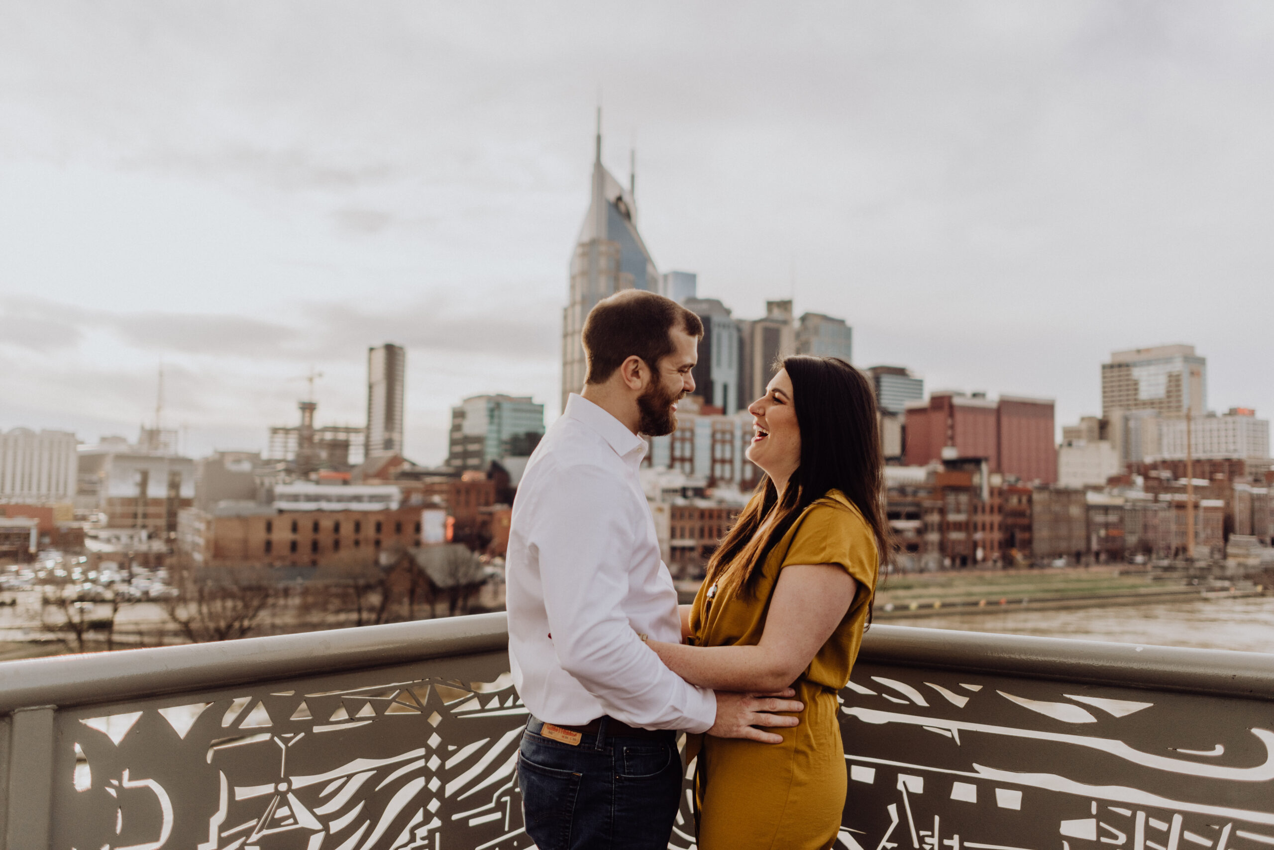 a man and woman laughing and looking at each other in front of the Nashville skyline during their engagement session