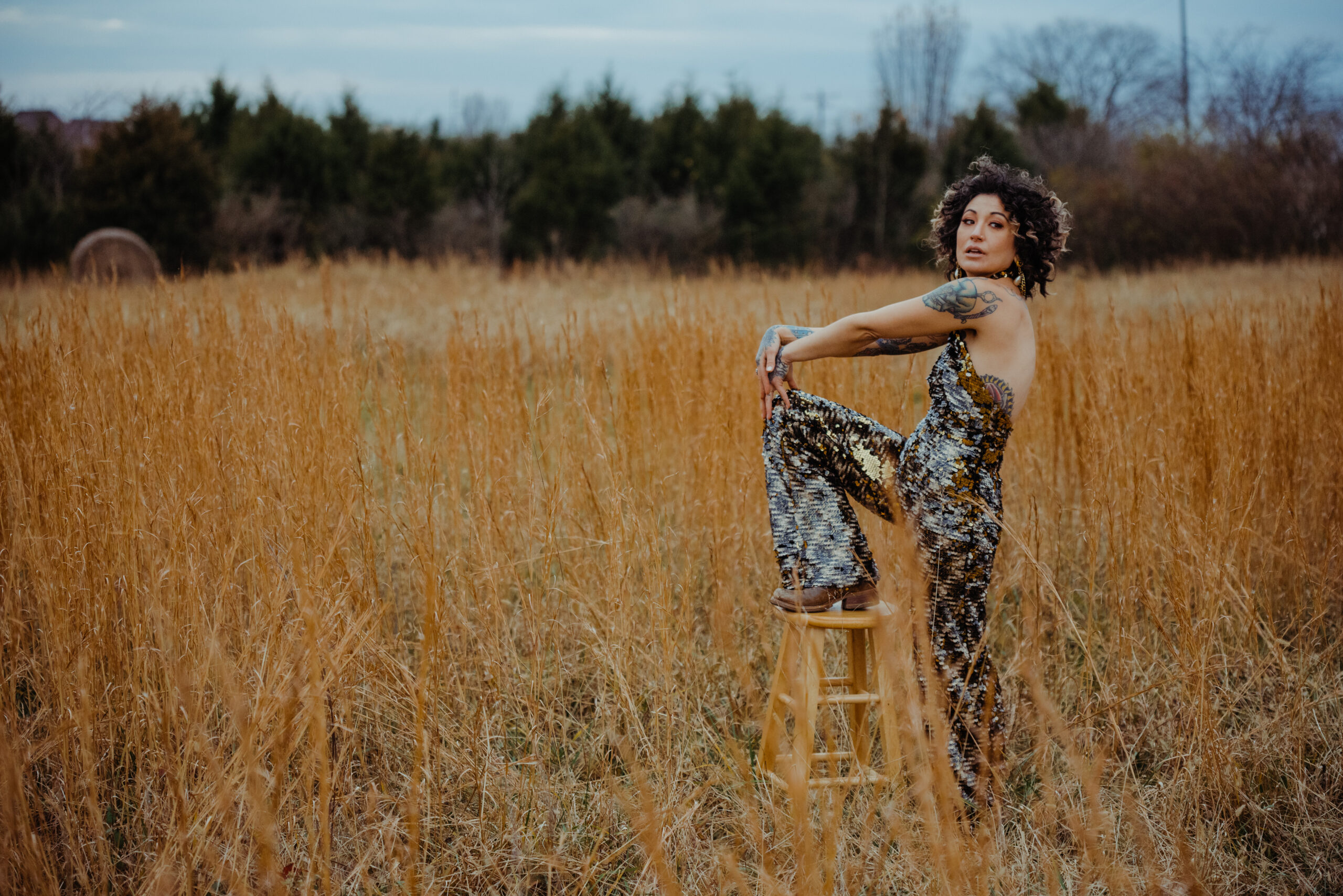 fashion editorial woman in a sequin jumpsuit with wild curly hair in a field of golden grass in nashville tn