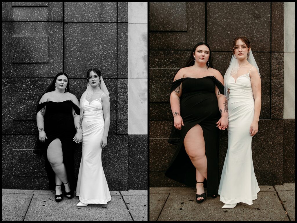 A lesbian couple stand side by side, holding hands against a stone wall, in what feels like the perfect wedding portrait. One wears a black dress with a high slit, and the other dons a white dress. The image is artfully split, one side in black and white and the other in color.