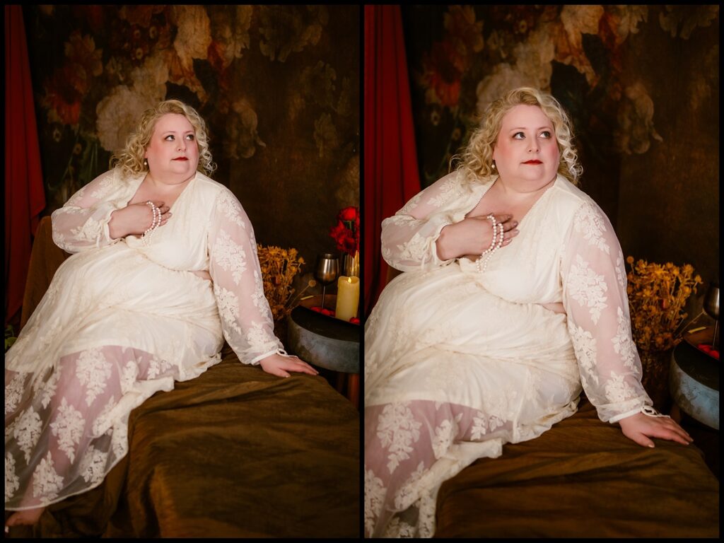 A person with curly blonde hair is seated on a brown surface against a dark, textured background. They wear a white lace dress and hold a pearl necklace. Flowers and a candle add to the dream-like ambiance, giving it an intimate, boudoir feel reminiscent of the Renaissance era.