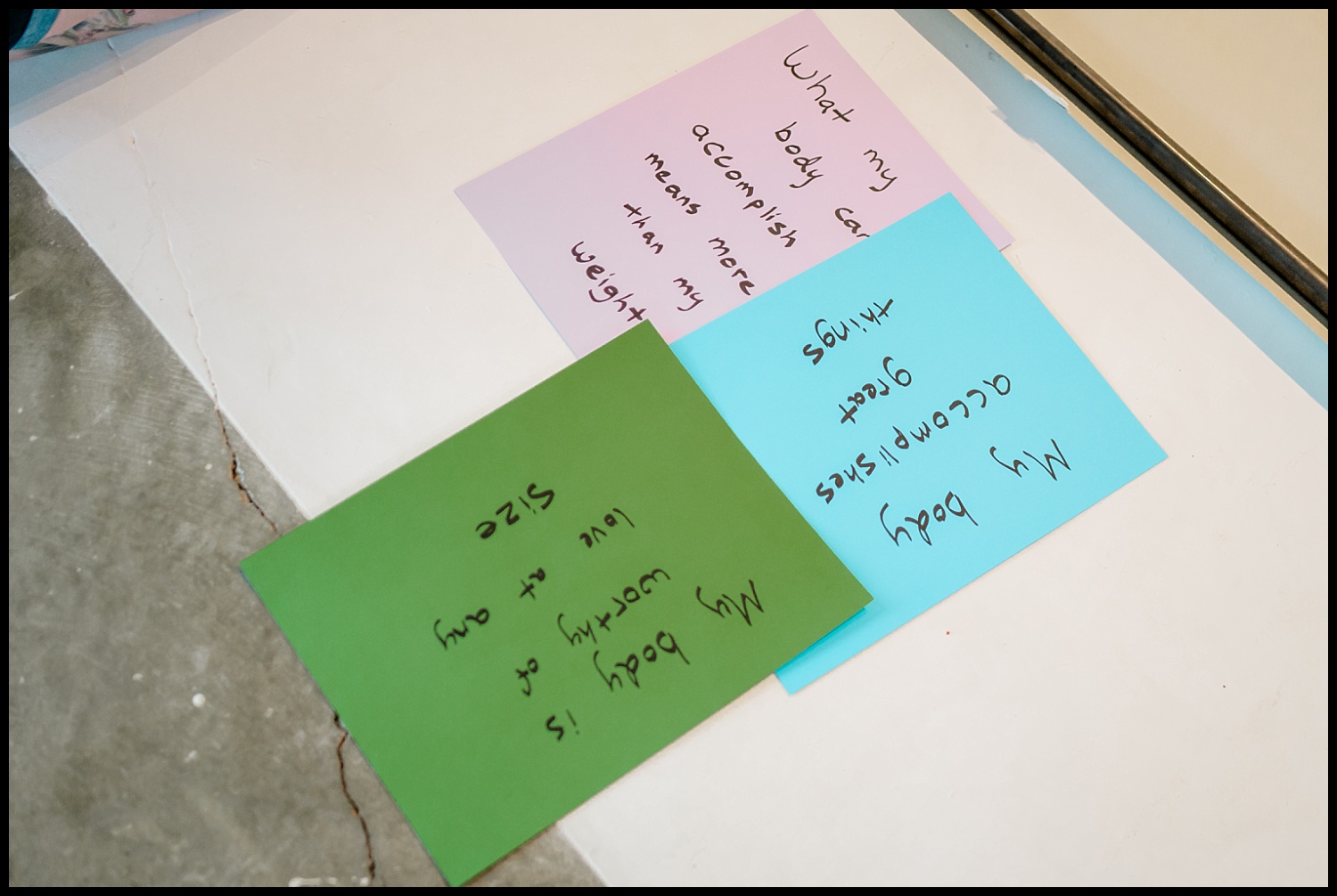 Three handwritten notes on colored paper read: “My body’s accomplishments matter more than my weight,” “My body accomplishes great things,” and “My body is worthy of love at any size”—powerful reminders of self-love and body acceptance.