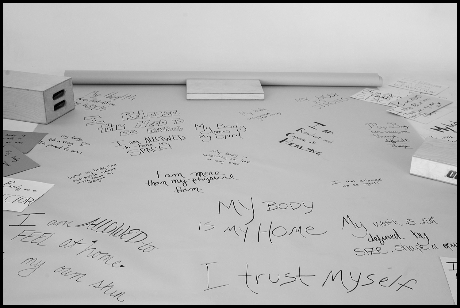 A tabletop covered with handwritten affirmations like MY BODY IS MY HOME and I trust myself, surrounded by pens, paper, and wooden blocks. This black-and-white Nashville Boudoir scene radiates self-love and empowerment.