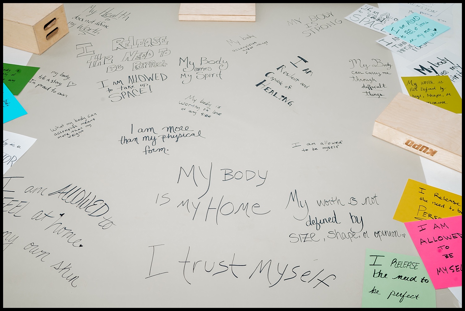 A tabletop covered with handwritten affirmations about body and self-acceptance, surrounded by colorful sticky notes and wooden blocks—perfect inspiration for a Nashville boudoir empowerment shoot focused on self-love.
