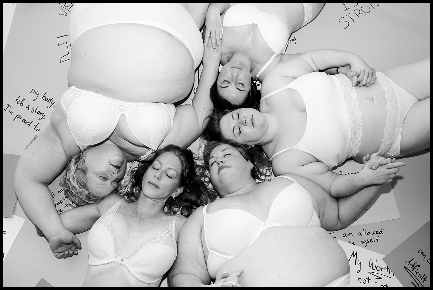 Five women in white bras and underwear lie in a circle, heads touching, eyes closed. Positive affirmations surround them on the floor. This black-and-white Nashville Boudoir empowerment shoot beautifully captures self-love and connection.