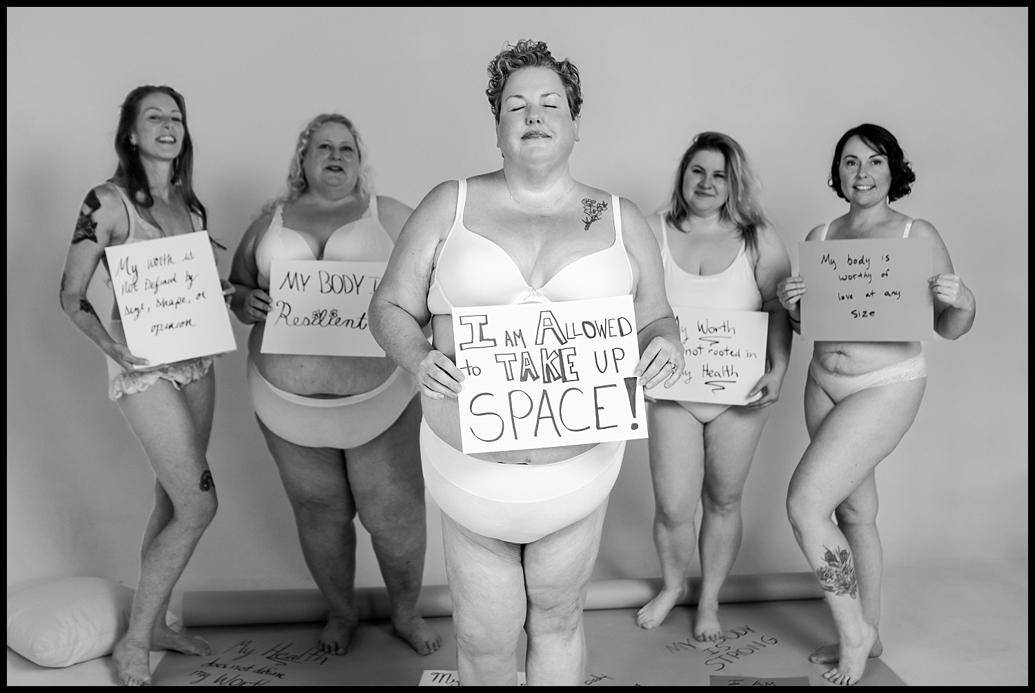 Five women in underwear stand confidently, holding body-positive signs with messages like I am allowed to take up space and My body is resilient, promoting self-love and diversity in this empowering Nashville boudoir shoot.