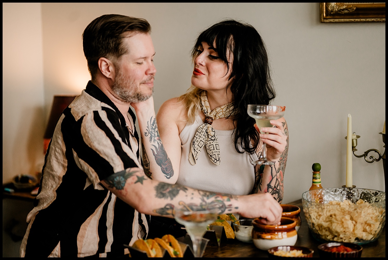 A man and woman sit closely at a table with tacos, chips, and drinks during their Couples Session. The woman smiles, holding a cocktail, while the man touches her face affectionately—a warm, intimate moment in Nashville.