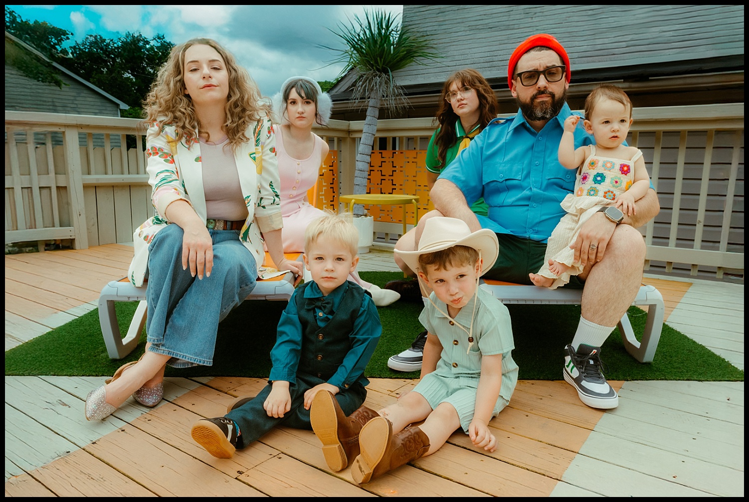 A group of people sitting on a deck, arranged like a Wes Anderson scene, evokes the charm of quirky family portraits in Nashville.