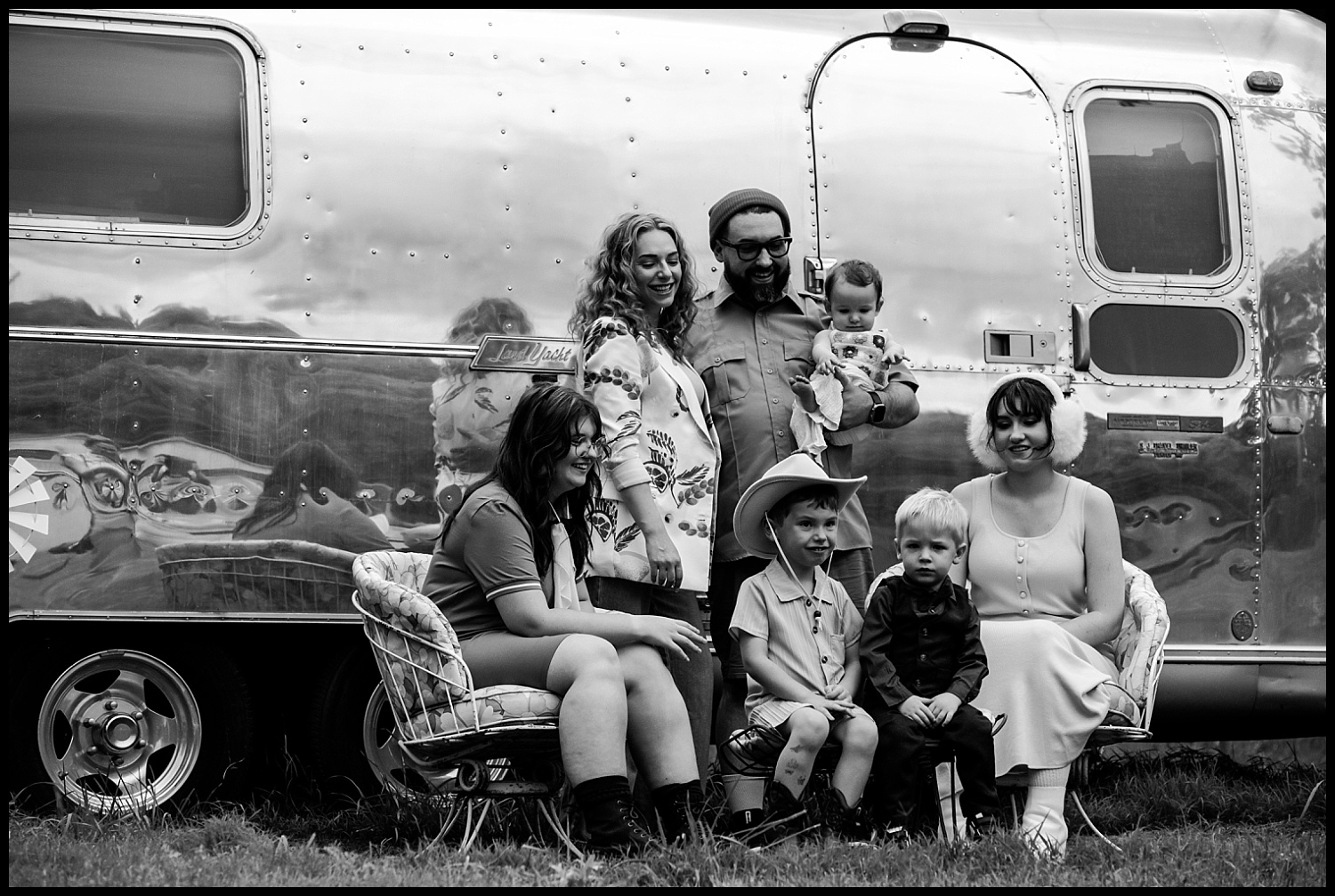 A black-and-white photo of a family with three adults and four children posing in front of a shiny Airstream trailer in Nashville. The group smiles and looks relaxed—a family portrait with subtle Wes Anderson vibes.