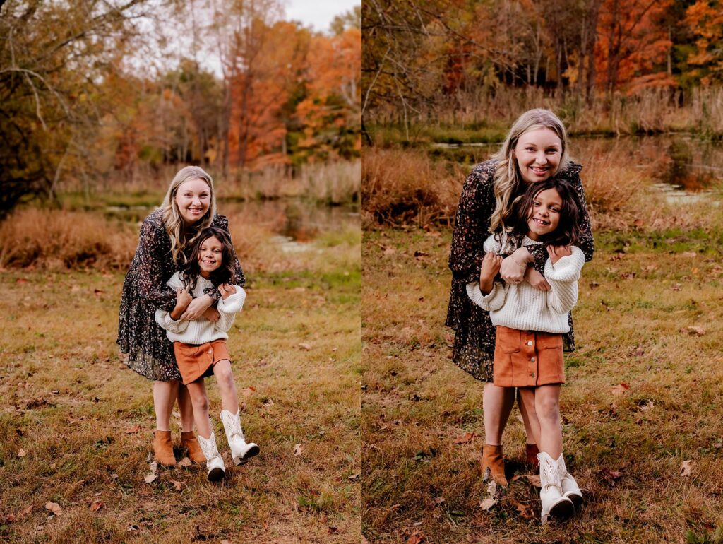 A woman and a young girl smile and pose together outdoors in a grassy area with autumn trees behind them during a Fall Family Session. Both wear fall outfits and boots, creating a perfect moment for family photography with a Nashville portrait photographer.