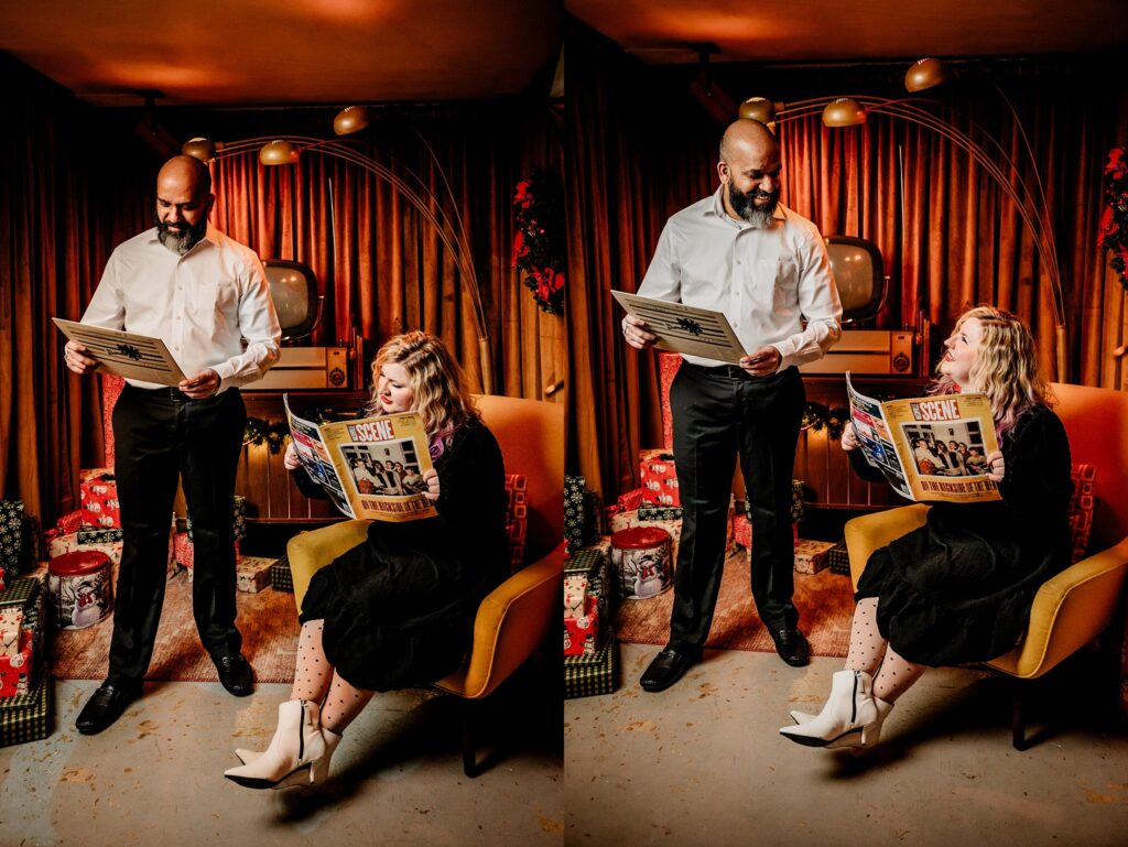A man stands holding a vinyl record, smiling at a seated woman with a Monkees album. In their retro-themed room, vintage Christmas décor and gifts surround them—capturing the joy of holiday photography in this cozy couples portrait session.