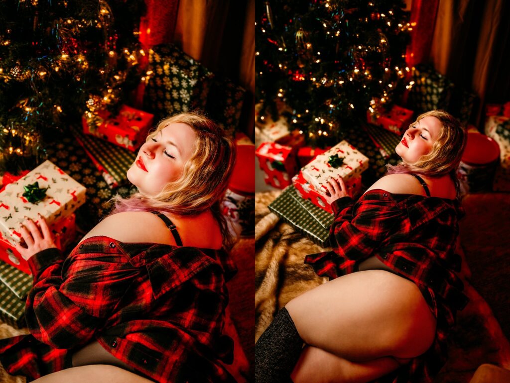A woman in a red plaid shirt poses sensually by a Christmas tree and wrapped gifts at a Nashville Boudoir Pop-Up Studio, with warm holiday lights creating a festive and intimate Vintage Christmas atmosphere.