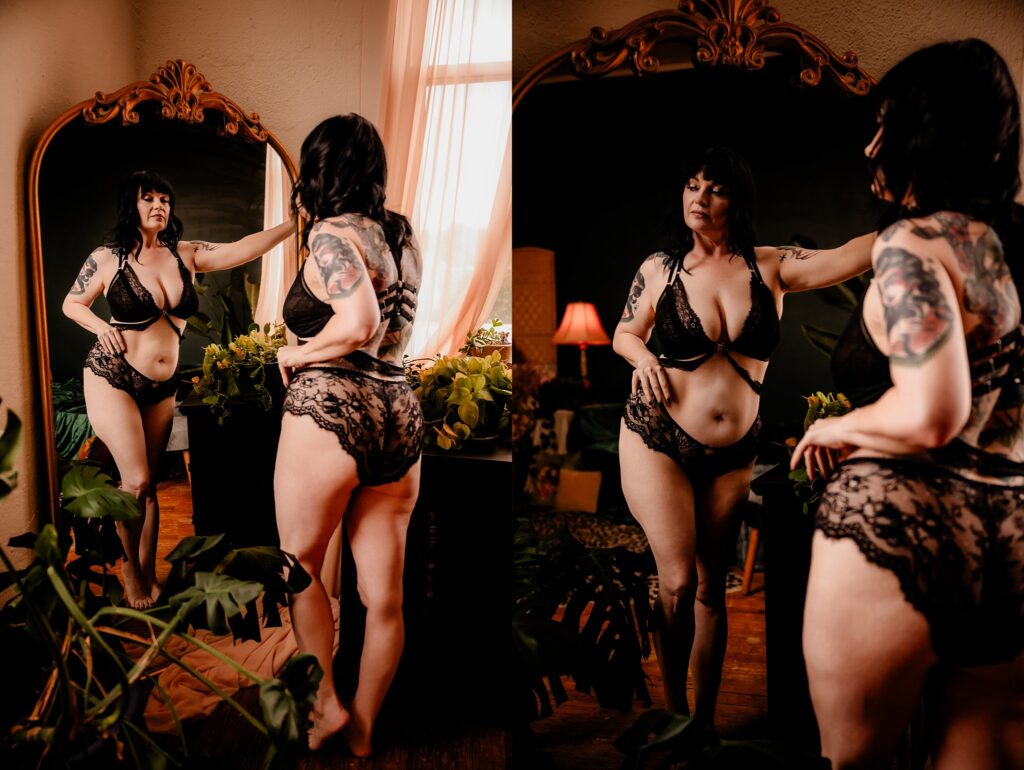 A woman in black lace lingerie stands in front of a large mirror in a warmly lit room with plants, soft light streaming in—capturing the elegance and intimacy found in Nashville Boudoir Photography.