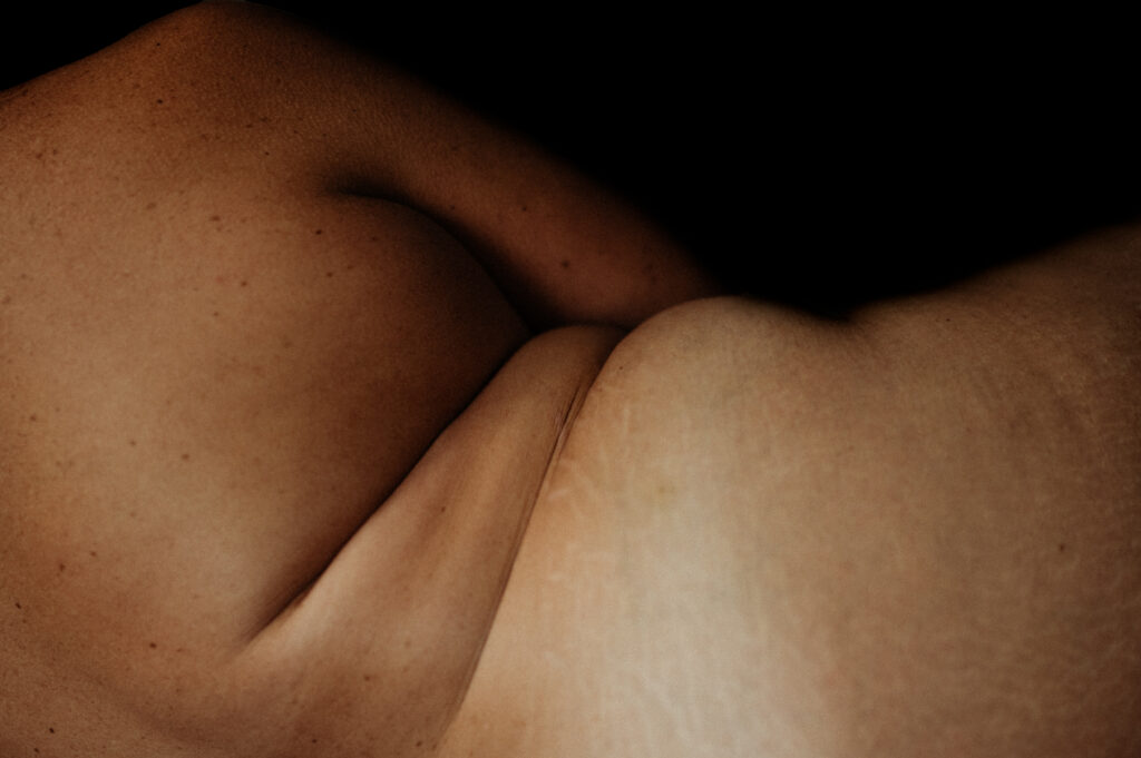Close-up image of a person’s bare torso and midsection, showing skin folds and natural texture against a dark background—a signature Nashville boudoir style with lighting that highlights the contours and variations in skin tone.