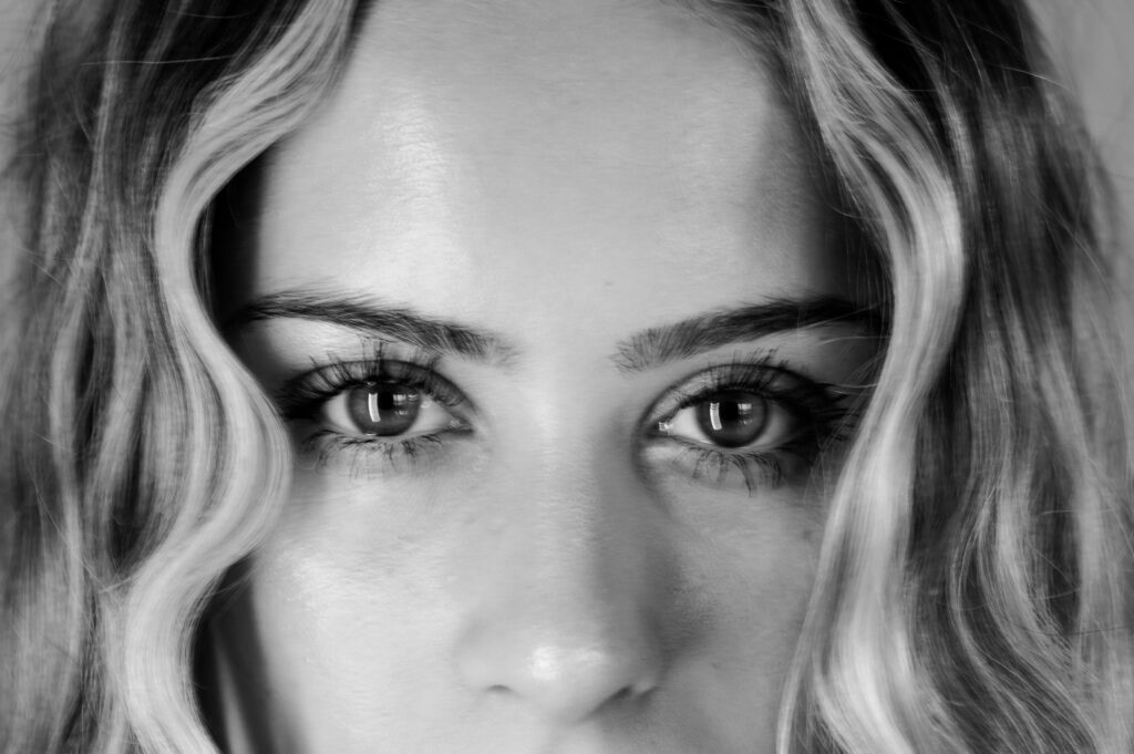 Black and white close-up of a woman’s face, her intense eyes and wavy hair framed by soft lighting, capturing the allure and elegance of Nashville boudoir photography.