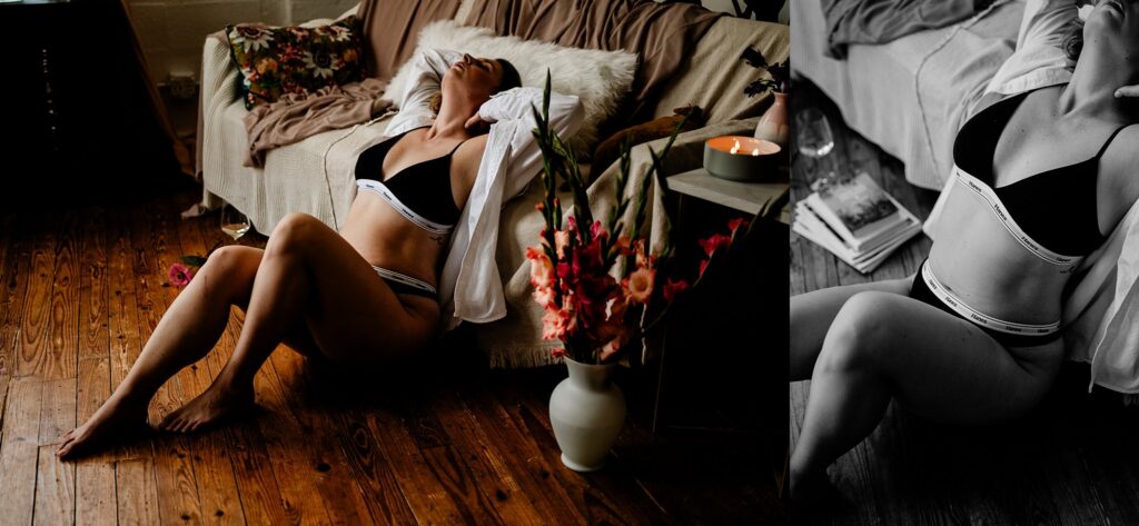A woman in black and white lingerie and an open shirt reclines on the floor by a couch, surrounded by flowers and soft lighting, capturing a relaxed, intimate bridal boudoir atmosphere.