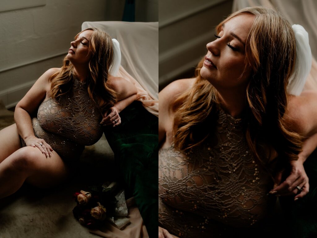 A woman with long hair poses in a sheer, beaded bodysuit, sitting and reclining against a dark green cushion. Soft light highlights her face as she gazes upward, capturing an elegant bridal boudoir vibe. Flowers rest on the floor nearby.