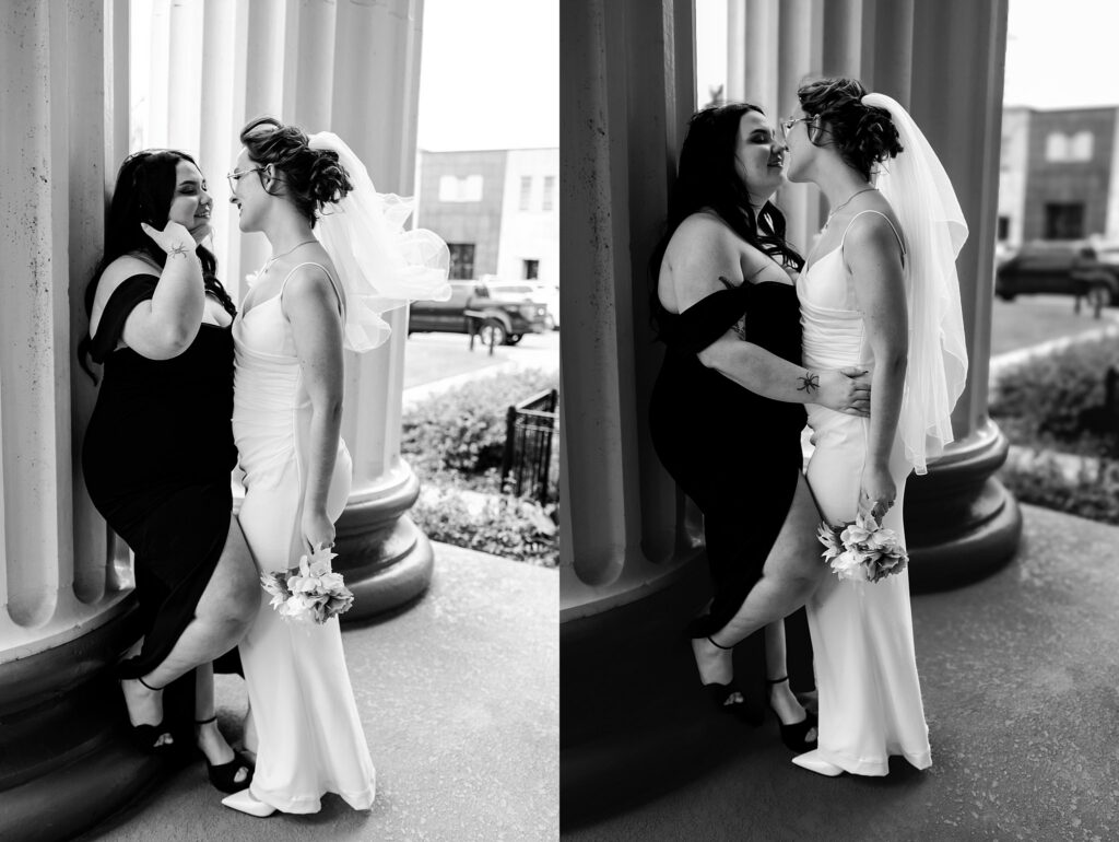Two women, one in a black dress and one in a white wedding gown with a veil, stand closely and affectionately near columns, smiling and touching noses in an outdoor setting captured by a Nashville wedding photographer.