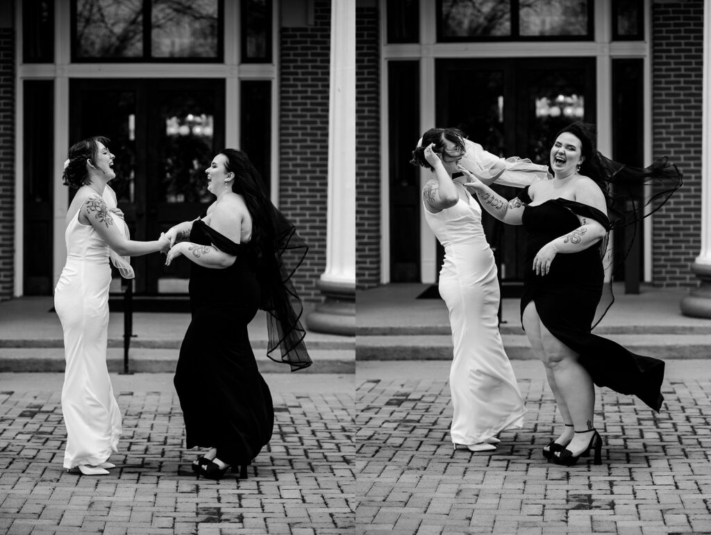 Two women, one in a white dress and one in a black dress, laugh and dance together outside a building with brick walls and columns. This joyful, candid moment is perfectly captured by a talented Nashville wedding photographer.