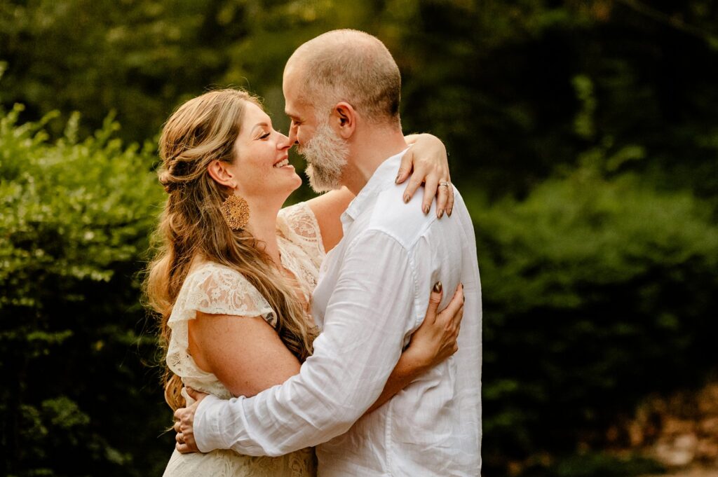 A couple in white clothing embraces outdoors, gazing at each other and smiling with greenery in the background, captured beautifully by a Nashville wedding photographer.