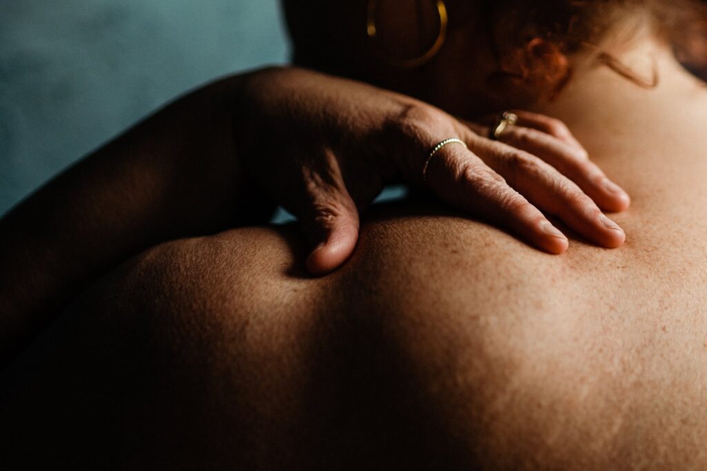 A close-up of a person’s bare back and shoulder, with their hand gently resting on the shoulder. Soft lighting highlights the skin's texture, creating a moody, intimate atmosphere—signature style of a Nashville creative portrait photographer.