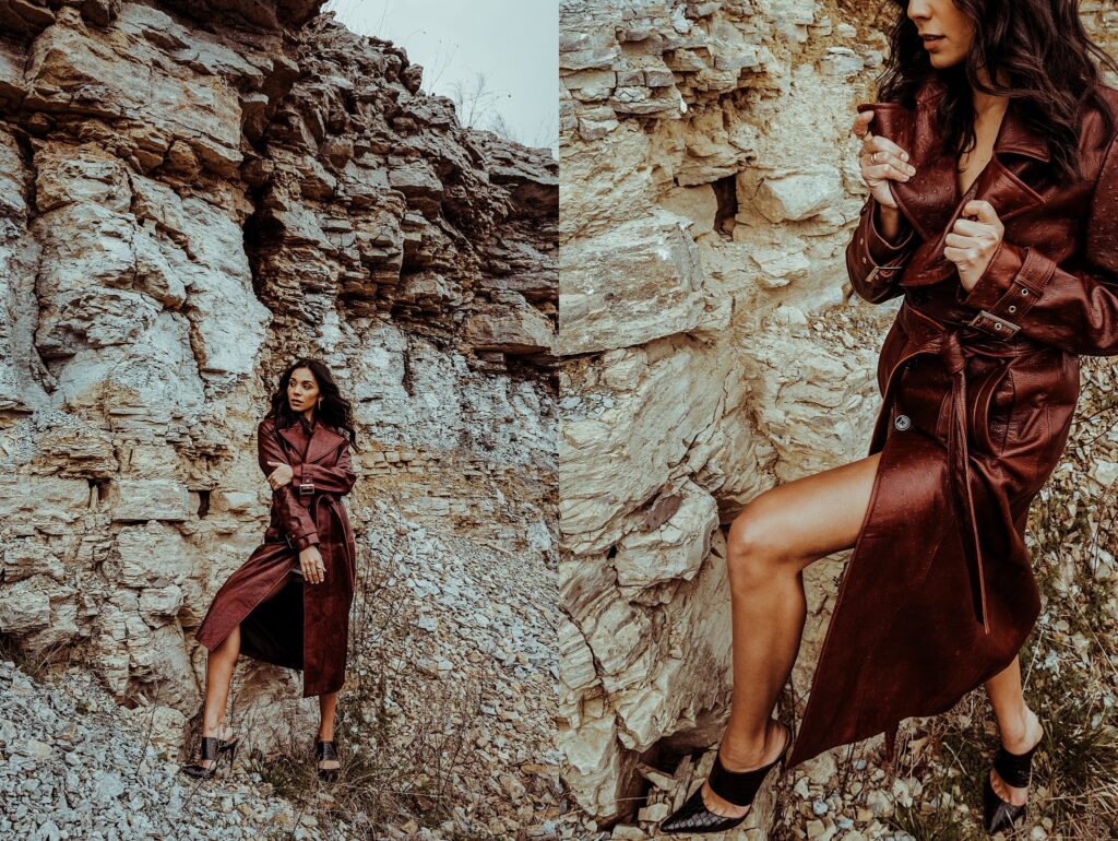 A woman in a long brown leather trench coat and black heels poses confidently against rugged cliffs, captured by a Nashville creative portrait photographer, with dry grass and overcast skies setting the scene.
