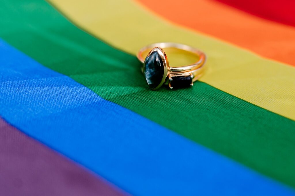 A gold ring with two gemstones rests on a colorful rainbow pride flag, representing LGBTQ+ pride and inclusivity—a perfect scene for a Nashville wedding photographer to capture love in all its forms.