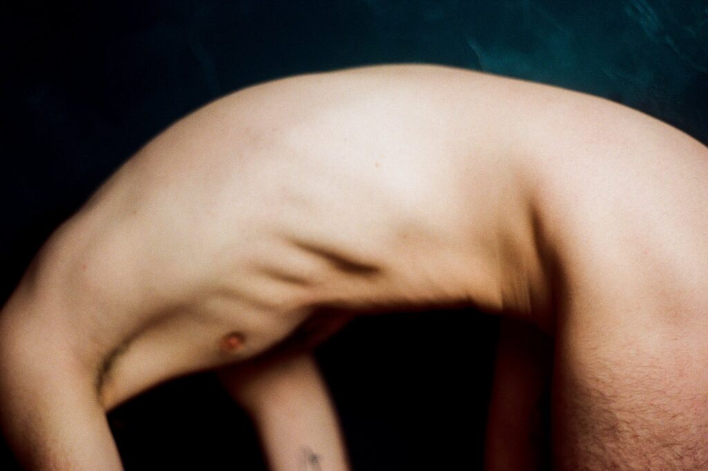 A blurred image by a Nashville creative portrait photographer, capturing a nude person bending backward, their torso and ribs prominently visible against a dark background.