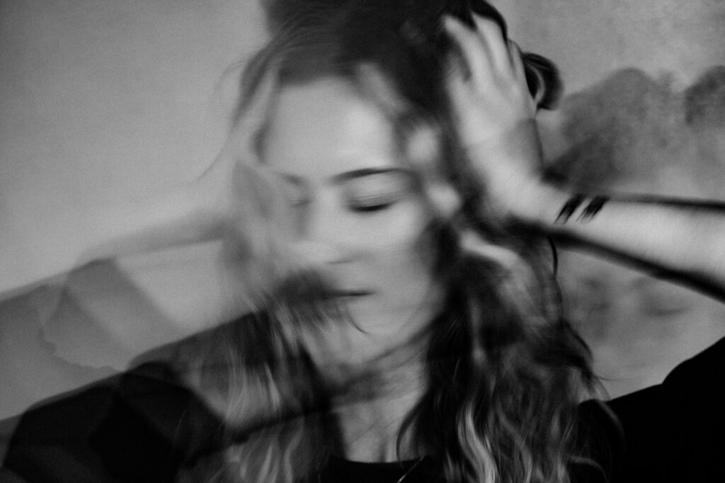 Black and white photo by a Nashville creative portrait photographer shows a person with long hair, head tilted down, hands on their head, in a blurred, double-exposure effect that conveys motion and emotional distress.