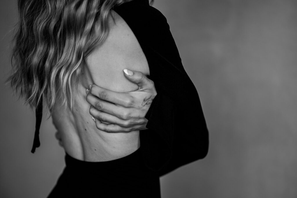 Black and white photo by a Nashville creative portrait photographer: a person with long wavy hair, in a black garment, holds their bare back; the focus on hand and back adds an intimate, artistic feel.