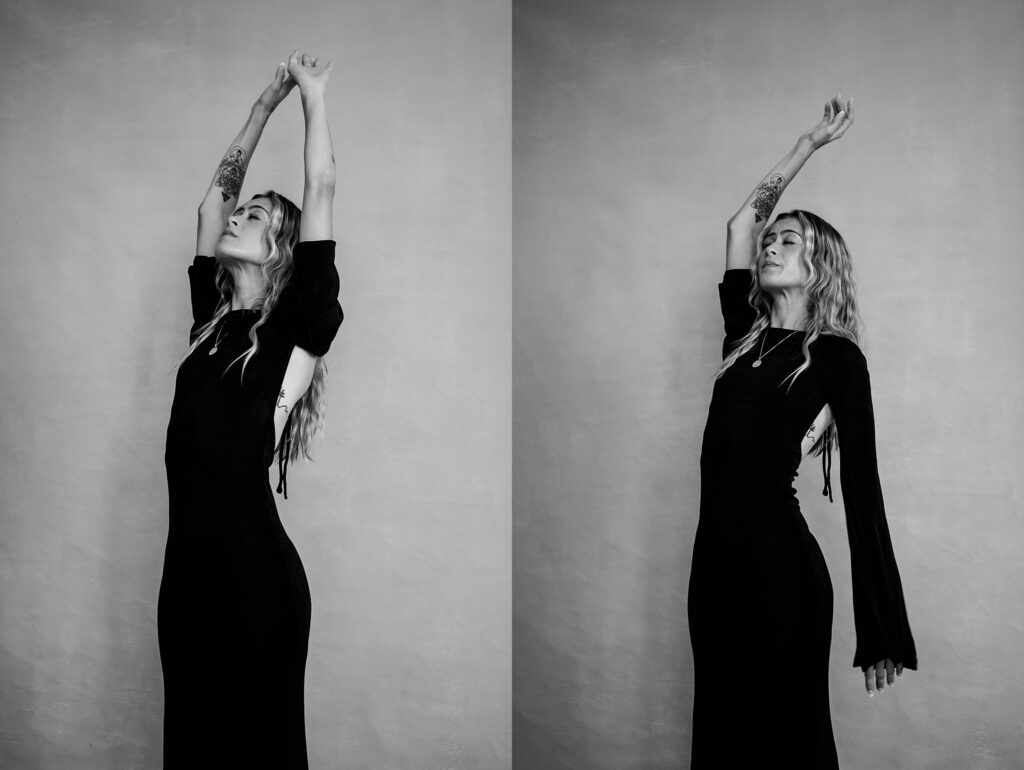 Black and white photo by a Nashville creative portrait photographer, featuring a woman in a long black dress with wavy hair and tattoos, standing against a plain backdrop, raising her arms overhead in two slightly different poses.