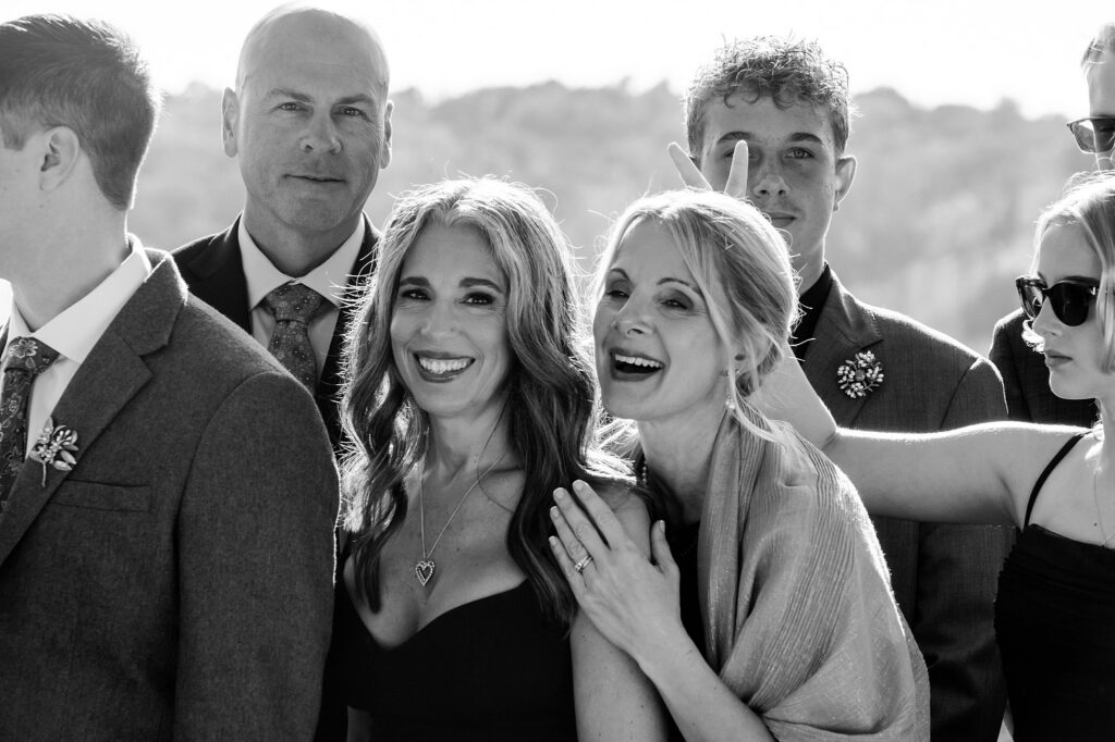 A group of people dressed formally pose for a photo outdoors, captured by a Nashville wedding photographer. Two women in front are smiling as a young man behind them playfully makes bunny ears. The mood is cheerful.