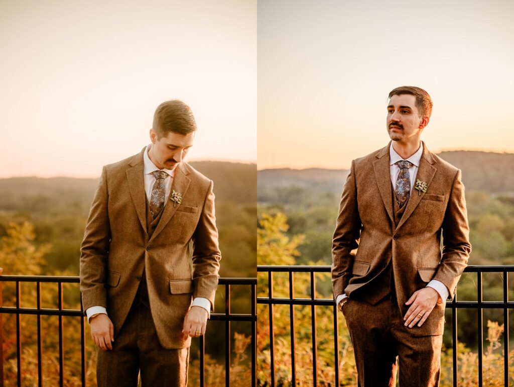 A man in a brown suit stands outside by a black railing, with a scenic landscape and sunset sky in the background. Captured by a Nashville wedding photographer, he poses with hands in pockets, looking down in one image and away in the other.