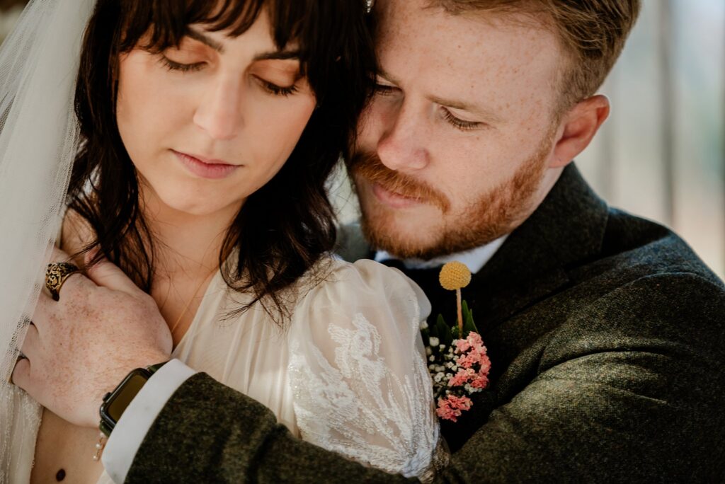 A bride and groom share a tender moment, with the groom gently embracing the bride from behind. Captured by a Nashville wedding photographer, their eyes are closed, appearing peaceful and close in wedding attire with floral accents.