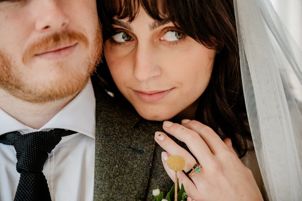 A bride with dark hair and veil rests her hand, showing her wedding ring, on the groom’s shoulder as she gazes softly at the camera—a timeless moment beautifully captured by a Nashville wedding photographer.