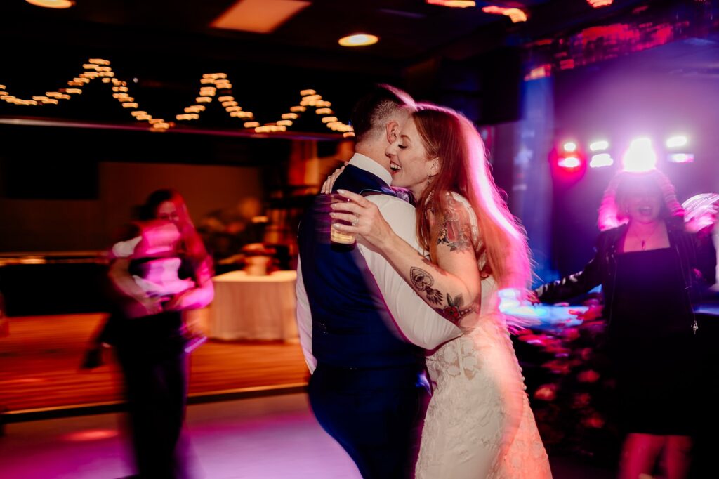 A bride and groom dance together, smiling and embracing on a colorful, festive dance floor as their Nashville wedding photographer captures the moment—blurred guests and string lights glowing in the background while the bride holds a drink to celebrate.