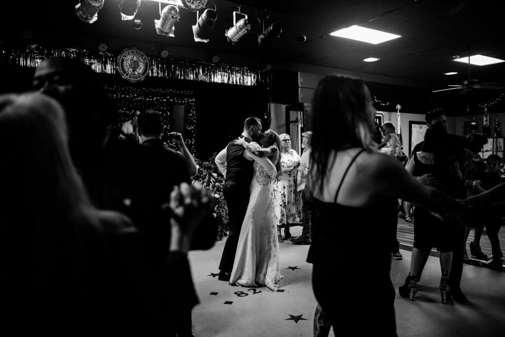 A couple in wedding attire shares a dance in the center of a dimly lit room, surrounded by other dancing couples and guests. Captured by a Nashville wedding photographer, the lively scene sparkles with string lights and festive decorations in the background.
