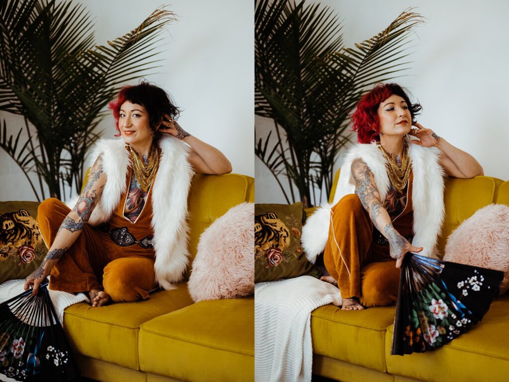 A woman with red hair and tattoos sits on a yellow couch, wearing a white fur vest and mustard outfit. Captured by a Nashville creative portrait photographer, she poses confidently with a black fan amid patterned cushions and potted plants.