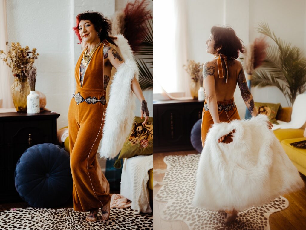 A woman in a mustard-yellow jumpsuit with a belt and tattoos poses indoors, holding a white faux fur coat. Captured by a Nashville creative portrait photographer, she stands on a cheetah-print rug amid bohemian decor, plants, and dried flowers.