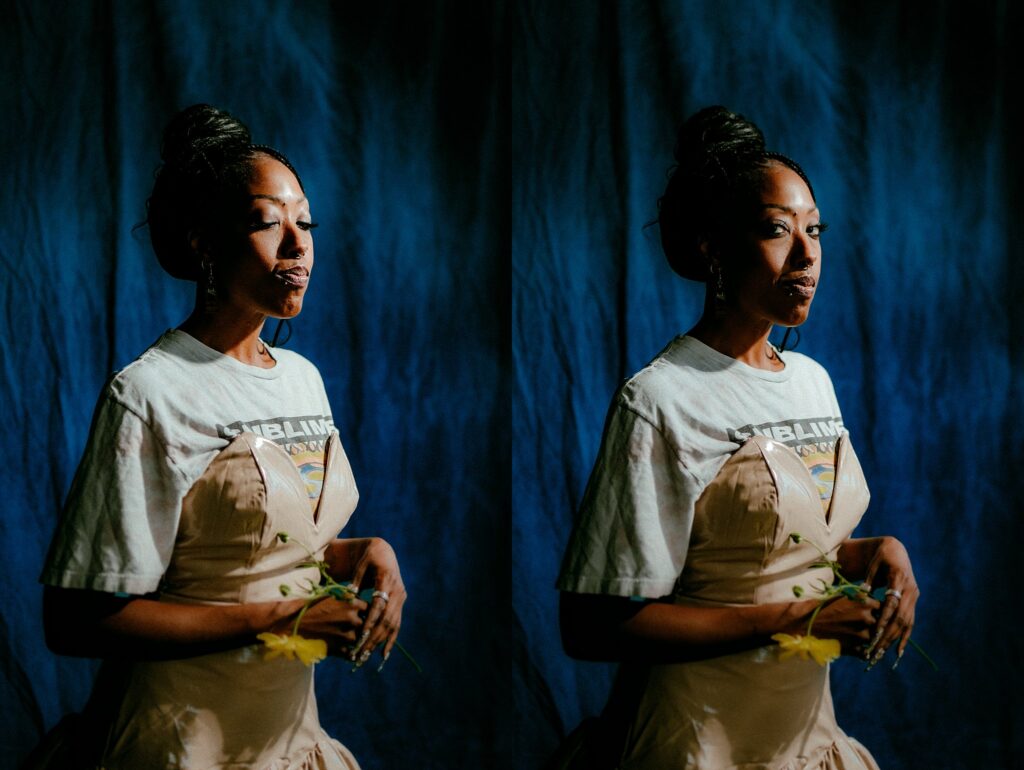 A woman stands against a dark blue backdrop, wearing a white graphic T-shirt over a light beige dress and holding yellow flowers. Captured by a Nashville creative portrait photographer, the image is duplicated side by side from slightly different angles.