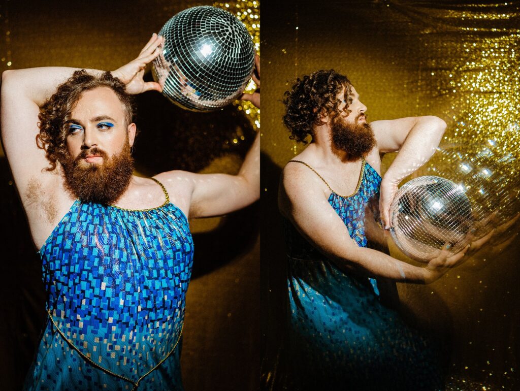 A bearded person in a blue, sequined dress poses with a disco ball against a sparkling gold background. Captured by a Nashville creative portrait photographer, they flaunt bold blue eye makeup and curly hair while striking expressive poses.